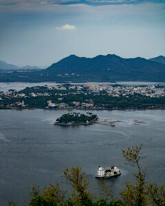 Scenic aerial view of Lake Pichola and surrounding landscapes in Udaipur, India, featuring mountains and islands.