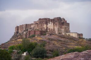 Scenic view of the iconic Mehrangarh Fort in Jodhpur, Rajasthan, showcasing historical architecture against a cloudy sky.