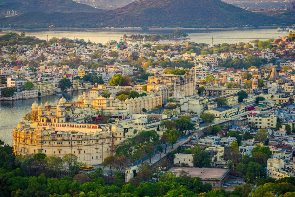 Aerial view of the historic Udaipur City Palace and surrounding cityscape against a tranquil lake backdrop.